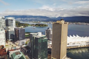 Downtown Vancouver seen from a tower. There are skyscrapers, a lake, a bridge and mountains in the background.