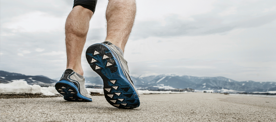 A man's legs as he's jogging towards snowy mountains in the distance.