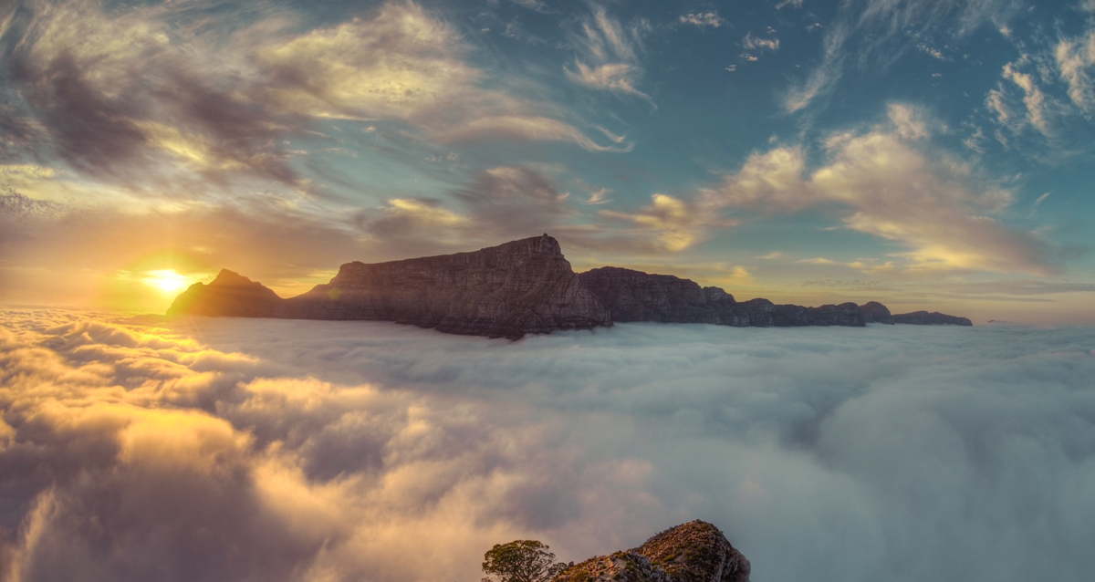 The sun rising behind Table Mountain in Cape Town. The mountain is above the clouds.