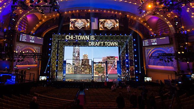 A mostly empty theater with many screens on and around the stage and a sign that says Chi Town is Draft Town.