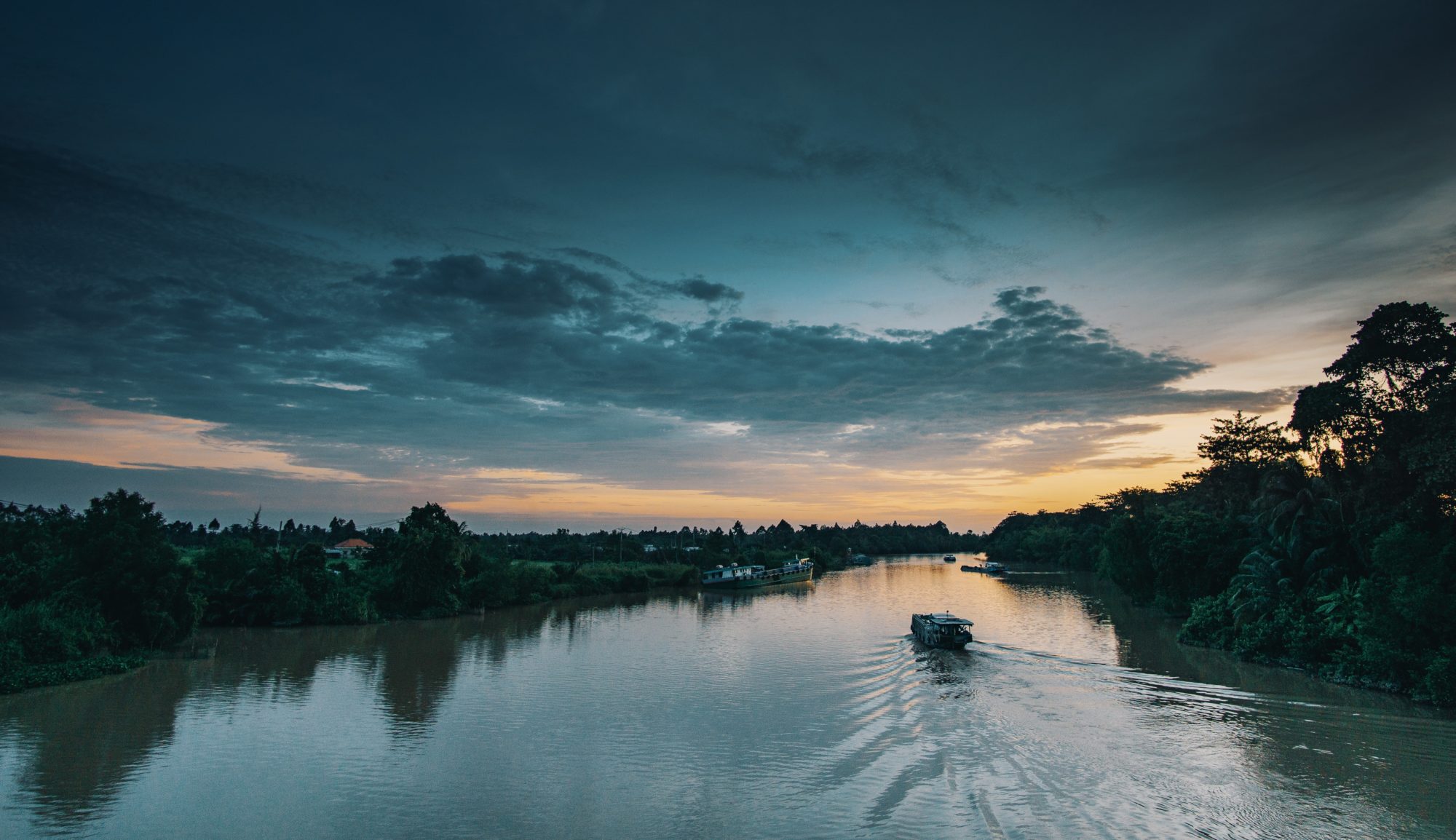 A tour boat going down a wide river at dusk.