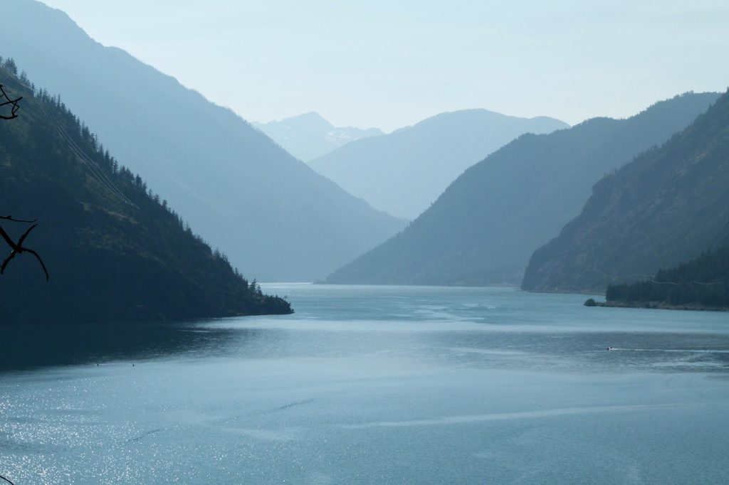 A lake with large hills on every side, in the fog.