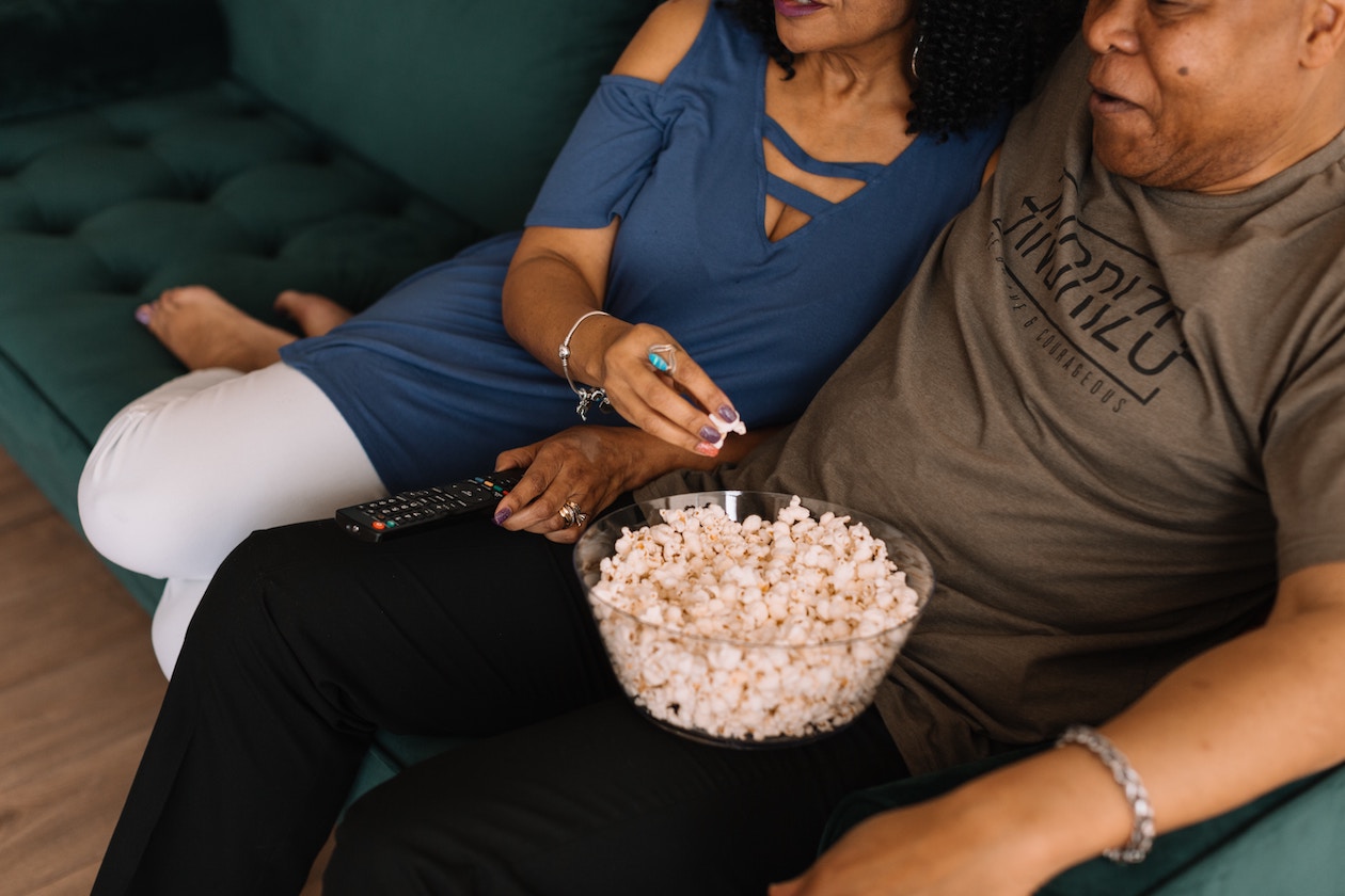A couple sitting together on a couch eating popcorn.