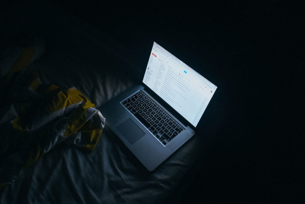 A laptop showing a gmail account. It sits on a bed in the dark.