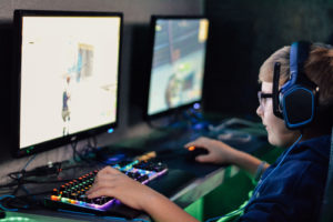 A little boy playing esports with 2 monitors.