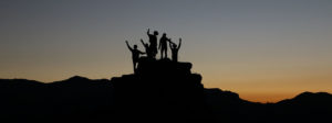 A group of people standing on an outcropping of rock while the sun has recently gone down behind them.